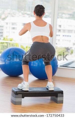 Full length rear view of a fit young woman exercising on step in gym