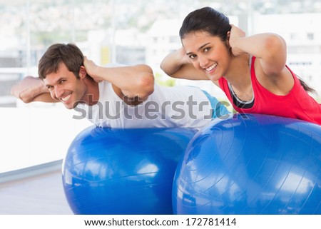 Fit young couple exercising on fitness balls in the bright gym