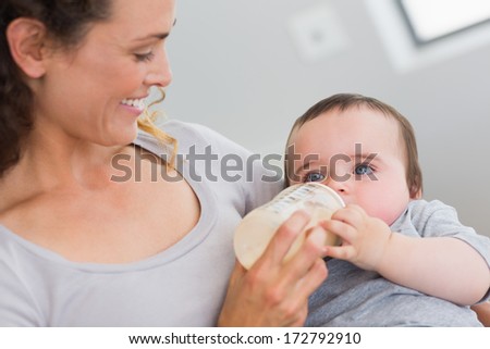 Smiling mother feeding milk to baby boy from bottle at home