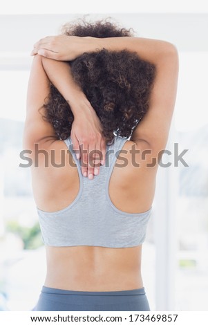 Rear view of a sporty young woman stretching hands behind back in fitness studio