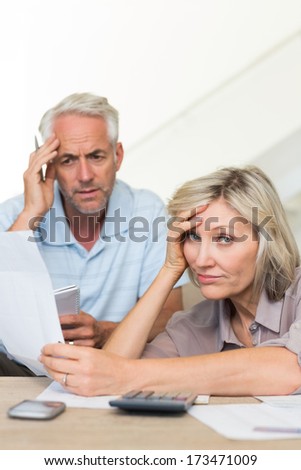 Tensed mature man and woman with bills sitting on sofa at home