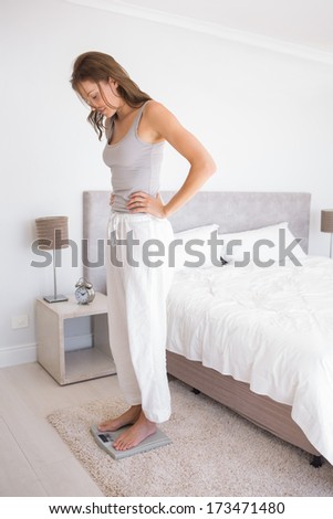 Full length side view of a fit young woman standing on scale in bedroom at home