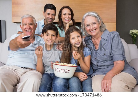 Portrait of happy extended family watching tv on sofa in the living room at home