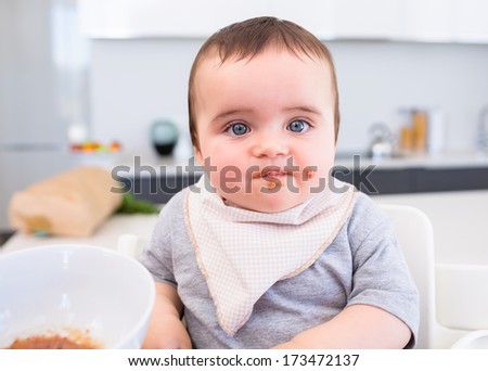 Portrait of messy baby boy eating food in kitchen