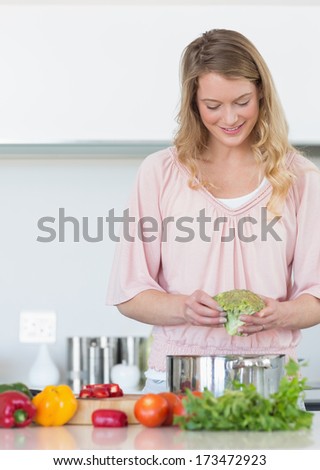 Smiling young woman preparing broccoli at kitchen counter