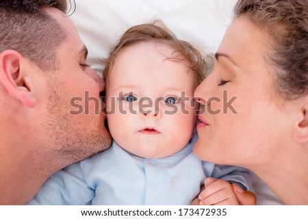High Angle Of Loving Parents Kissing Baby Boy In Bed