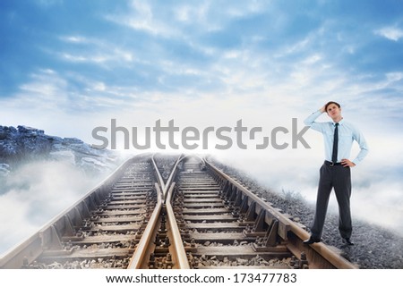 Thoughtful businessman with hand on head against railway tracks leading to clouds