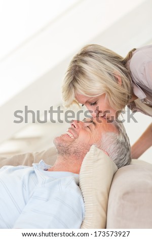 Side view of a woman kissing a relaxed mature man\'s forehead in the living room at home