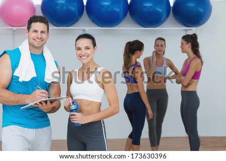 Portrait of a smiling couple with fitness class in background at gym