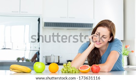 Smiling young woman with fruits on counter in the kitchen at home