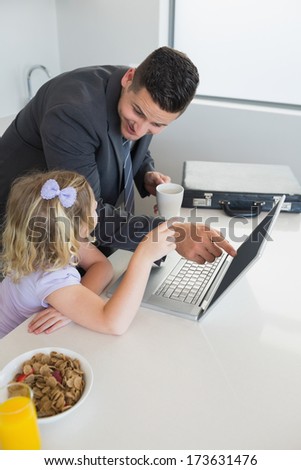 Businessman pointing at laptop while looking at daughter during breakfast