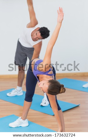 Sporty young couple stretching hands at yoga class in fitness studio