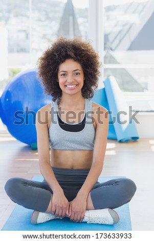 Full length portrait of a fit young woman sitting on exercise mat in a bright fitness studio