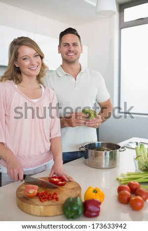 Portrait of happy couple cooking vegetables together at kitchen counter