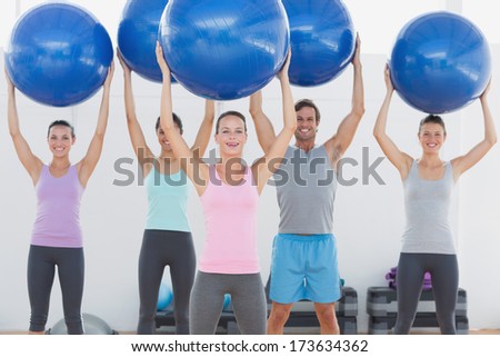 Portrait of an instructor and fitness class holding up exercise balls at the fitness studio