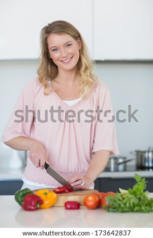 Portrait of young woman slicing vegetables on chopping board at kitchen counter