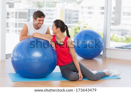 Portrait of a smiling fit young couple with exercise ball sitting at a bright gym