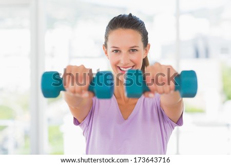 Portrait of a smiling young woman lifting dumbbell weights in a bright gym