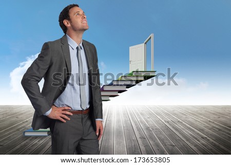 Smiling businessman with hand on hip against book steps against sky