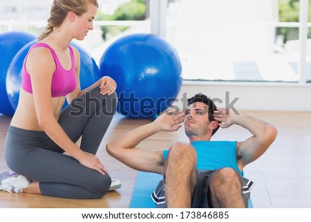 Side view of female trainer helping man with his exercises at a bright gym
