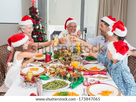 Happy family in santas hats toasting wine glasses at dining table in the house