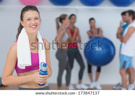 Portrait of a fit female holding water bottle with fitness class in background at gym