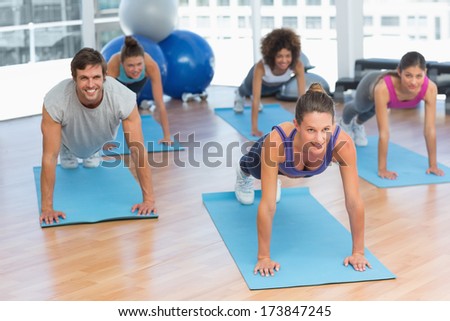 Smiling young people doing push ups in the fitness studio