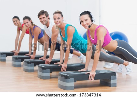 Side view portrait of instructor with fitness class doing step aerobics exercise in a gym