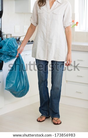 Low section of a young woman carrying garbage bag in the kitchen at house