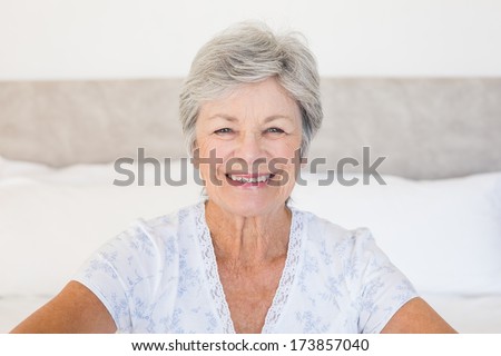 Portrait of happy senior woman sitting on bed at home