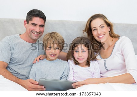 Portrait Of Smiling Family With Digital Tablet In Bed