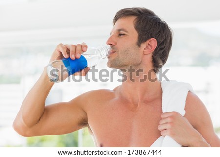 Shirtless young man with towel drinking water in the gym