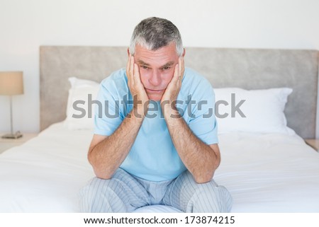 Portrait of sad senior man with head in hands sitting on bed at home