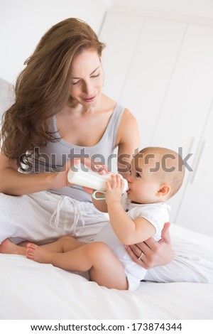 Mother feeding baby with milk bottle in bed at home