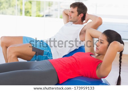 Side view of a fit young couple exercising on fitness balls in the bright gym