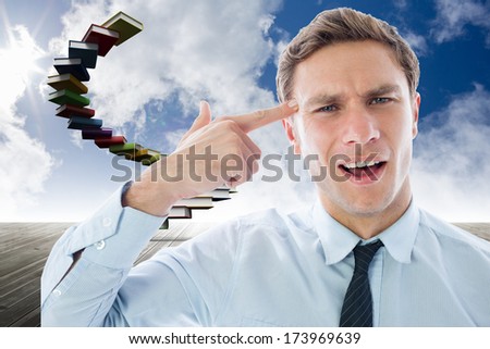 Businessman making gun gesture against book steps against sky