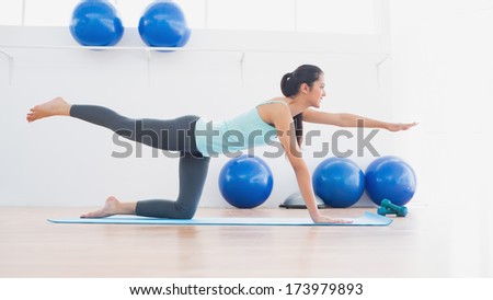 Side view of a sporty young woman stretching hand and leg in fitness studio