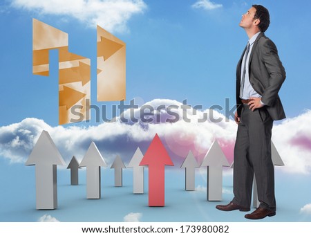 Serious businessman with hand on hip against red and grey arrows pointing up against sky
