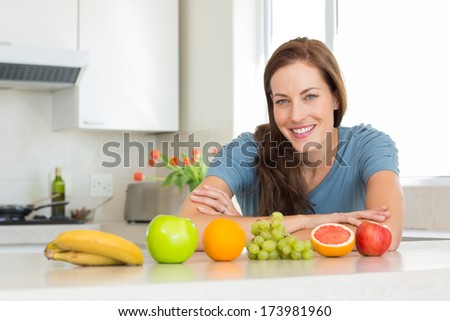 Portrait of a smiling young woman with fruits on counter in the kitchen at home