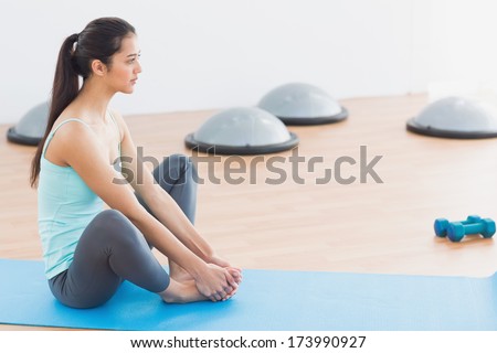 Side view of a fit young woman doing the butterfly stretch in exercise room