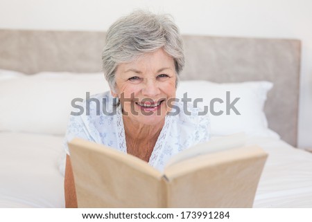 Portrait of happy senior woman reading story book while lying in bed