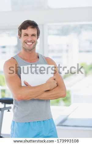 Portrait of a fit young man standing with scale in a bright exercise room