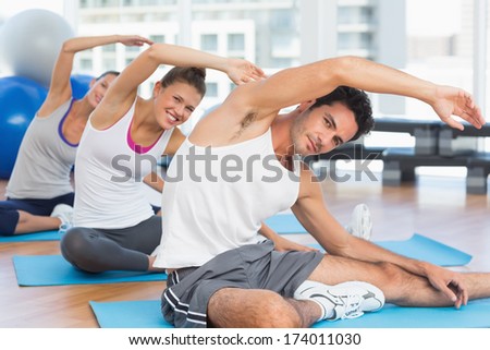Three sporty people stretching hands at yoga class in fitness studio