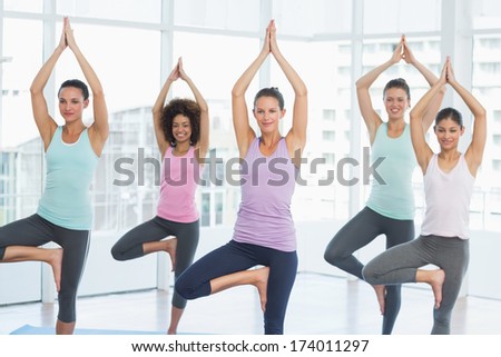 Portrait of a fit class standing in tree pose at a bright fitness studio