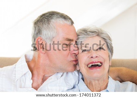 Senior man kissing happy wife sitting on sofa at home