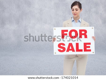Estate agent holding for sale sign against grey room