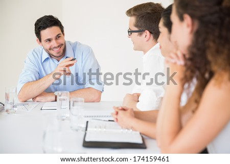 Smiling young businessman pointing at colleague during meeting in office