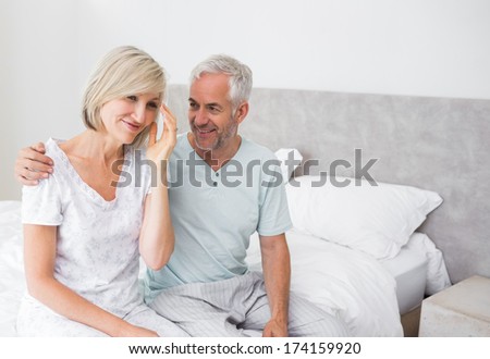 Smiling mature man and woman sitting on bed at home