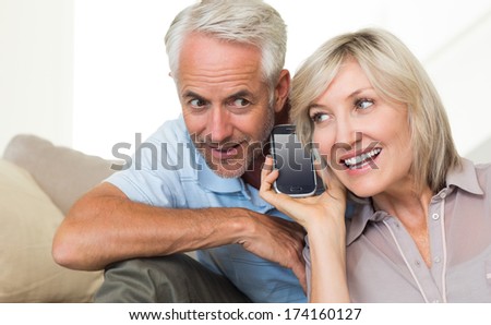 Smiling mature man and woman using a smartphone on sofa at home