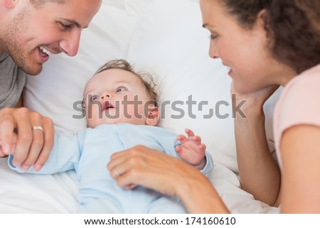 Loving parents looking at baby boy lying in bed